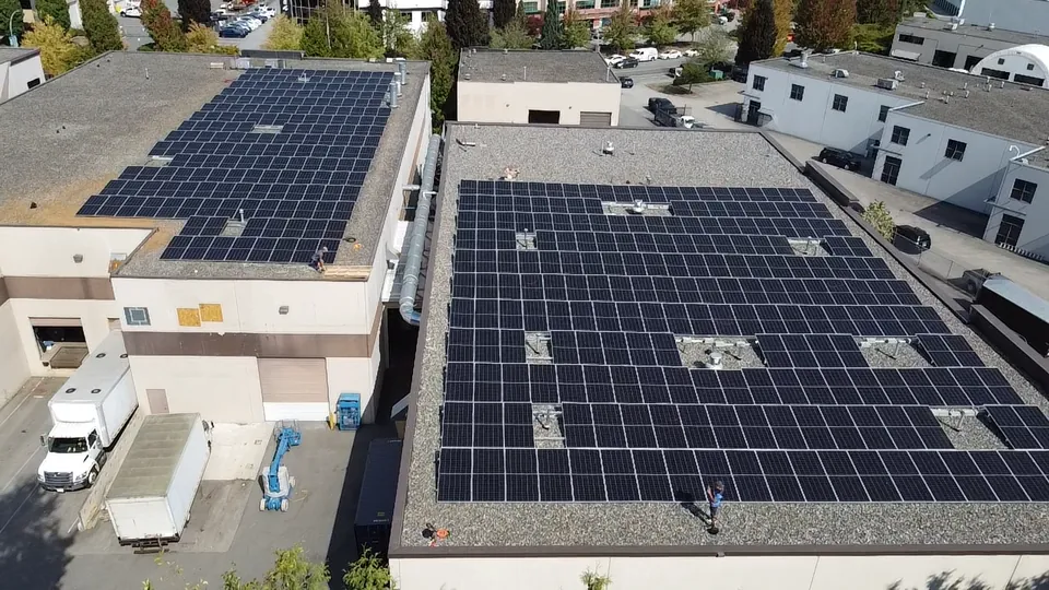 Aerial view of large solar arrays across the flat gravel roofs of two commercial buildings in the Lower Mainland