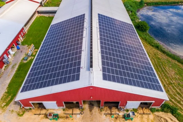 Solar panels covering both slopes of a long red agricultural barn roof