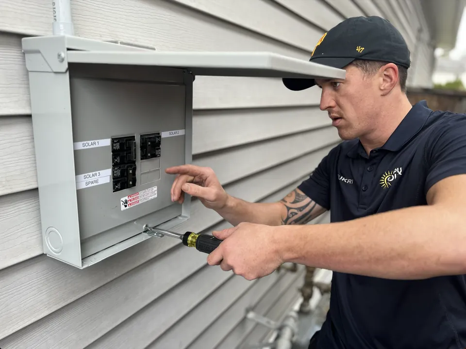 A Pure Solar electrician working in an electrical panel on the side of a house